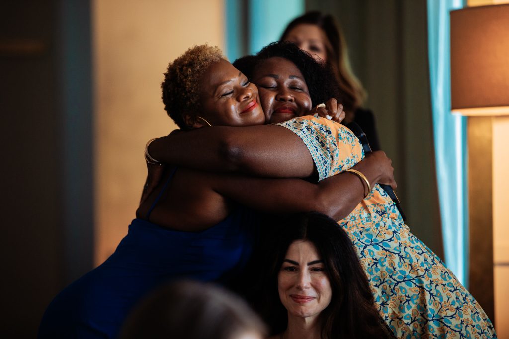 Two women hugging warmly at a Hello Seven event